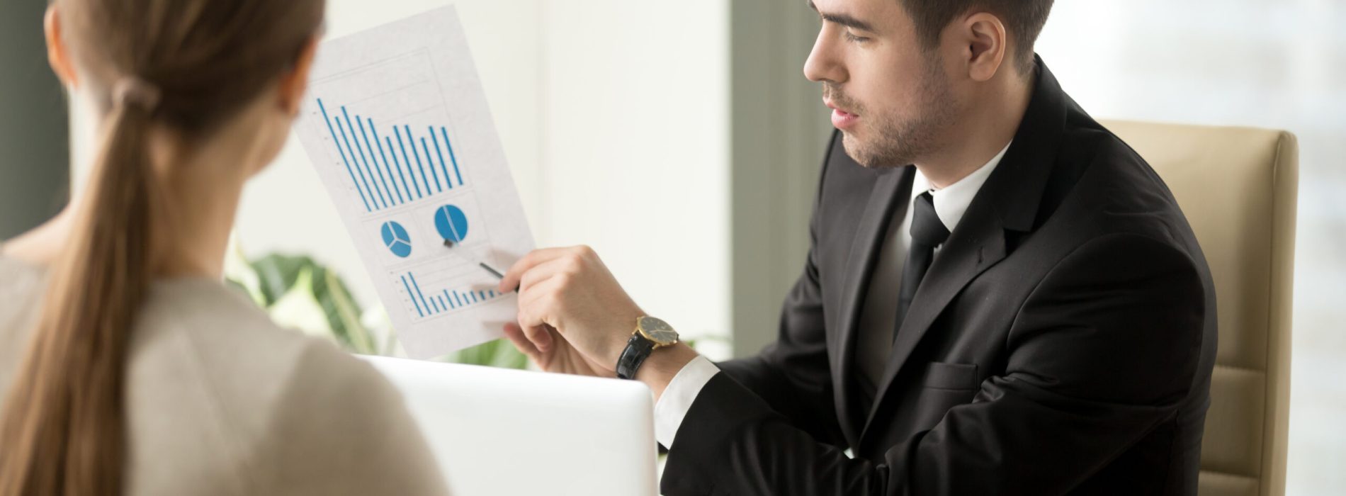 Male financial adviser showing document with profitability forecast to female client. Bank employee explaining terms of loan agreement and interest rate to borrower. Business plan presentation concept