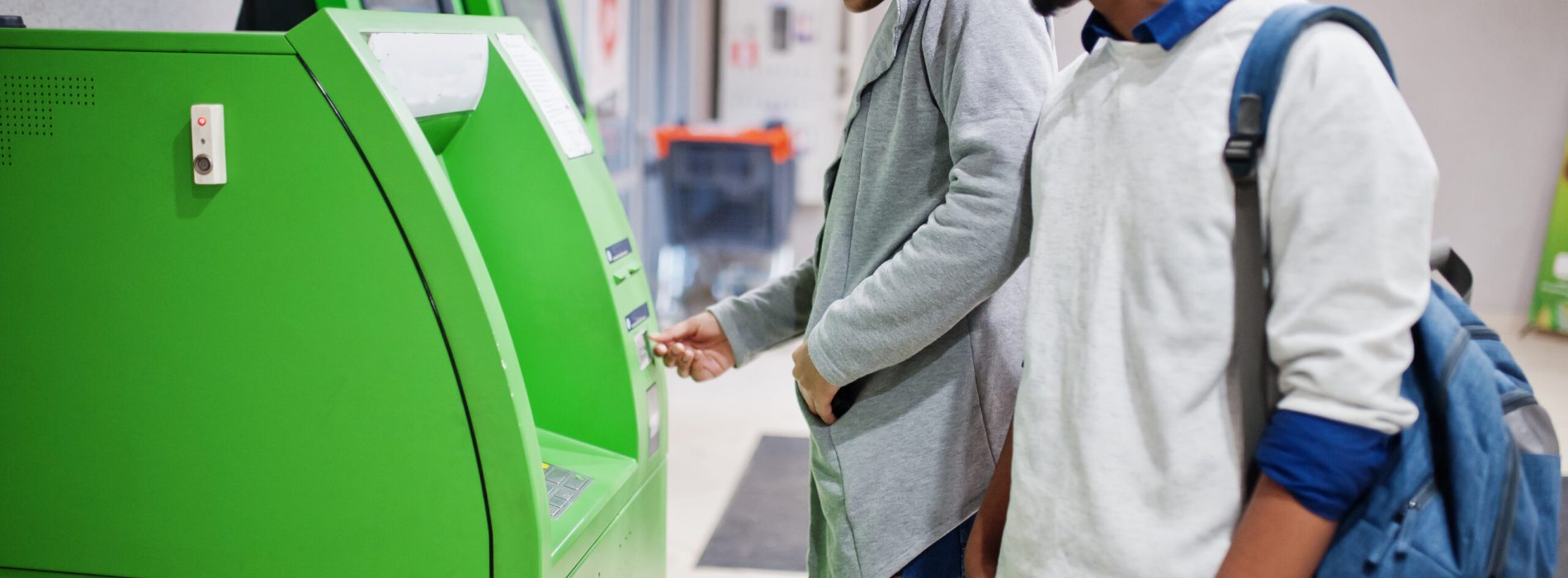 Two asian guys removes cash from an green ATM.